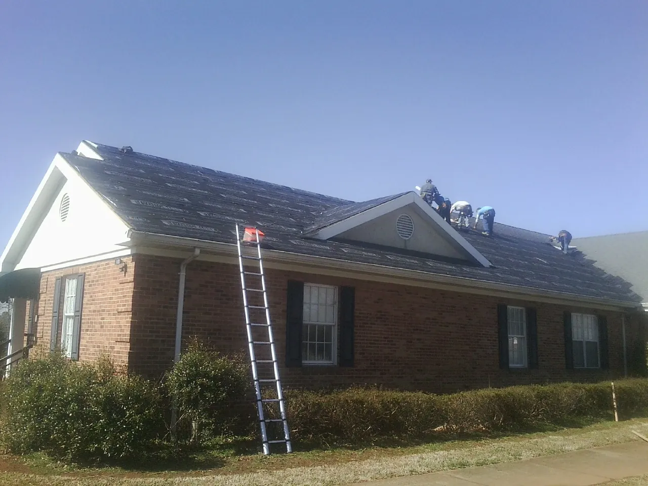 Crew tearing shingles off a brick ranch roof with a ladder set — Emergency Roof Repair work by our crew in Tetonia