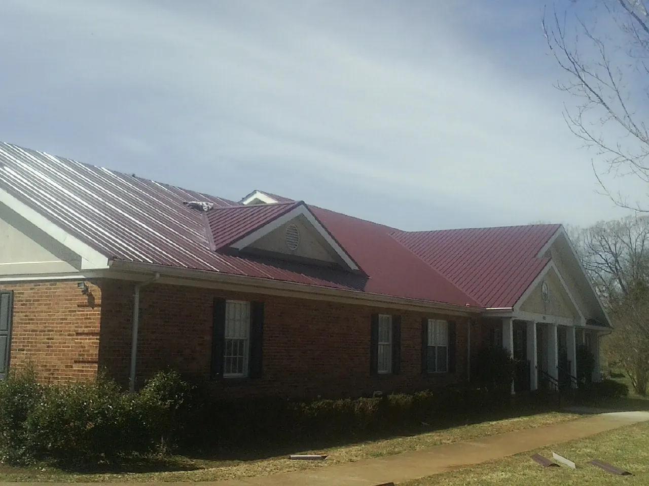 Red metal roof with gabled entries on a long brick building, from a Hail Damage Roof Repair job in Tetonia