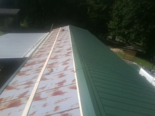 Old rusted panels beside newly installed green metal roofing — Wind Damage Roof Repair by Roofing Brothers in Tetonia