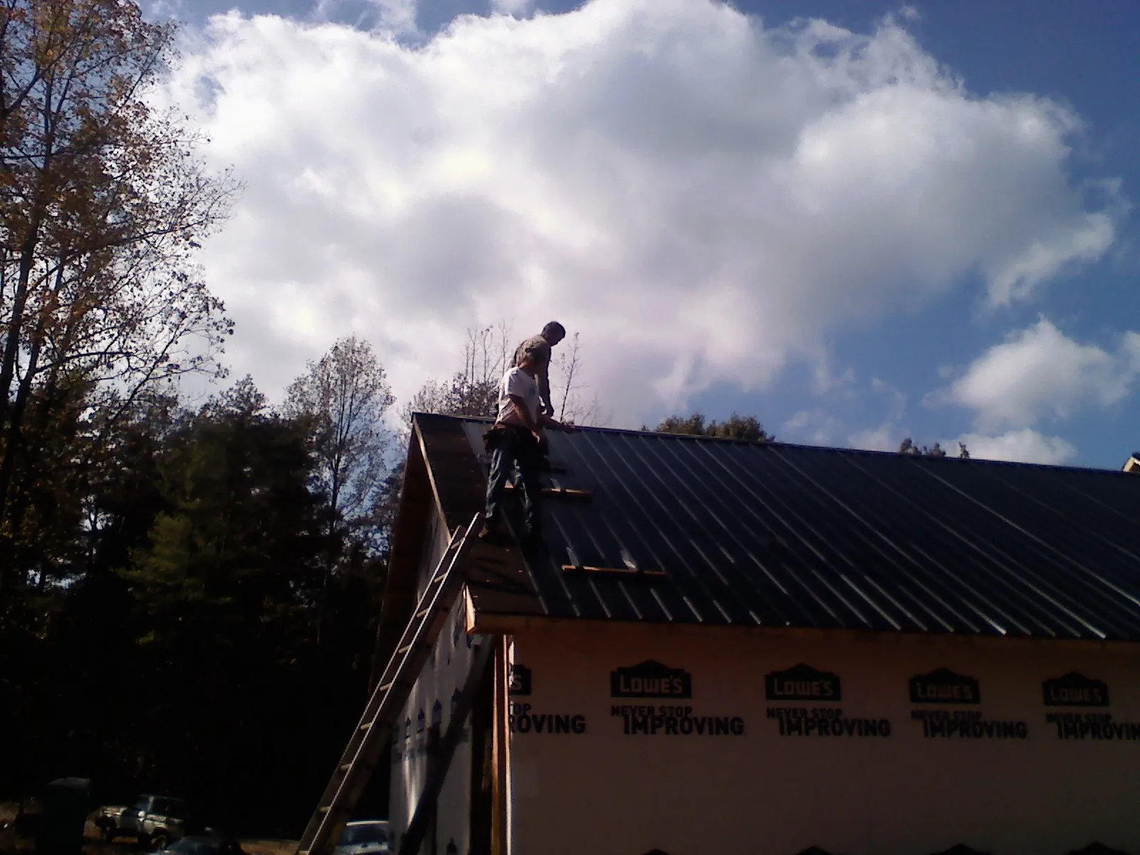 Roofer fastening dark metal panels high against a cloudy sky, from a Roof Inspection job in Tetonia