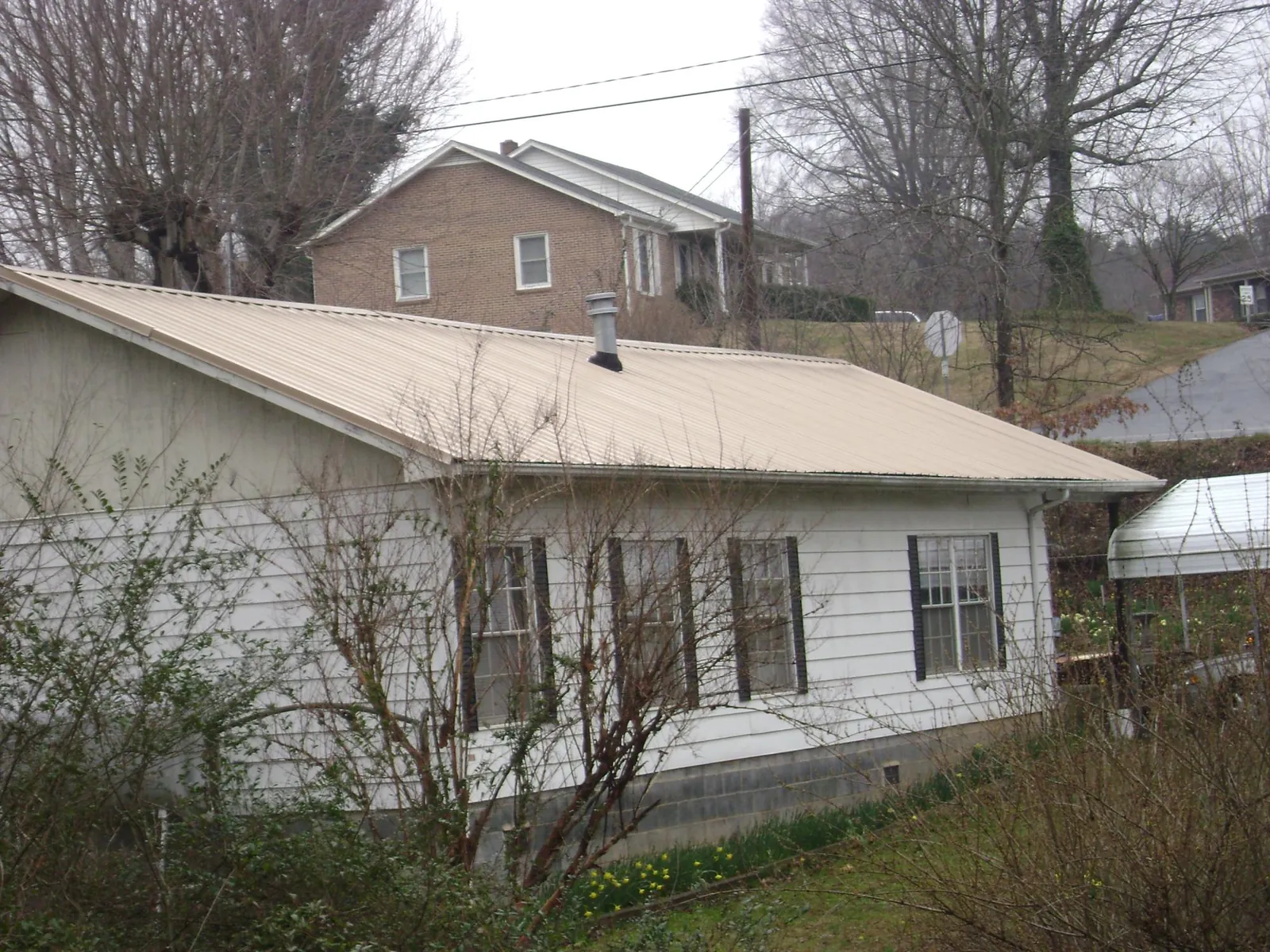 Tan metal roof on a white sided house set into a hillside — Commercial Roofing by Roofing Brothers in Tetonia
