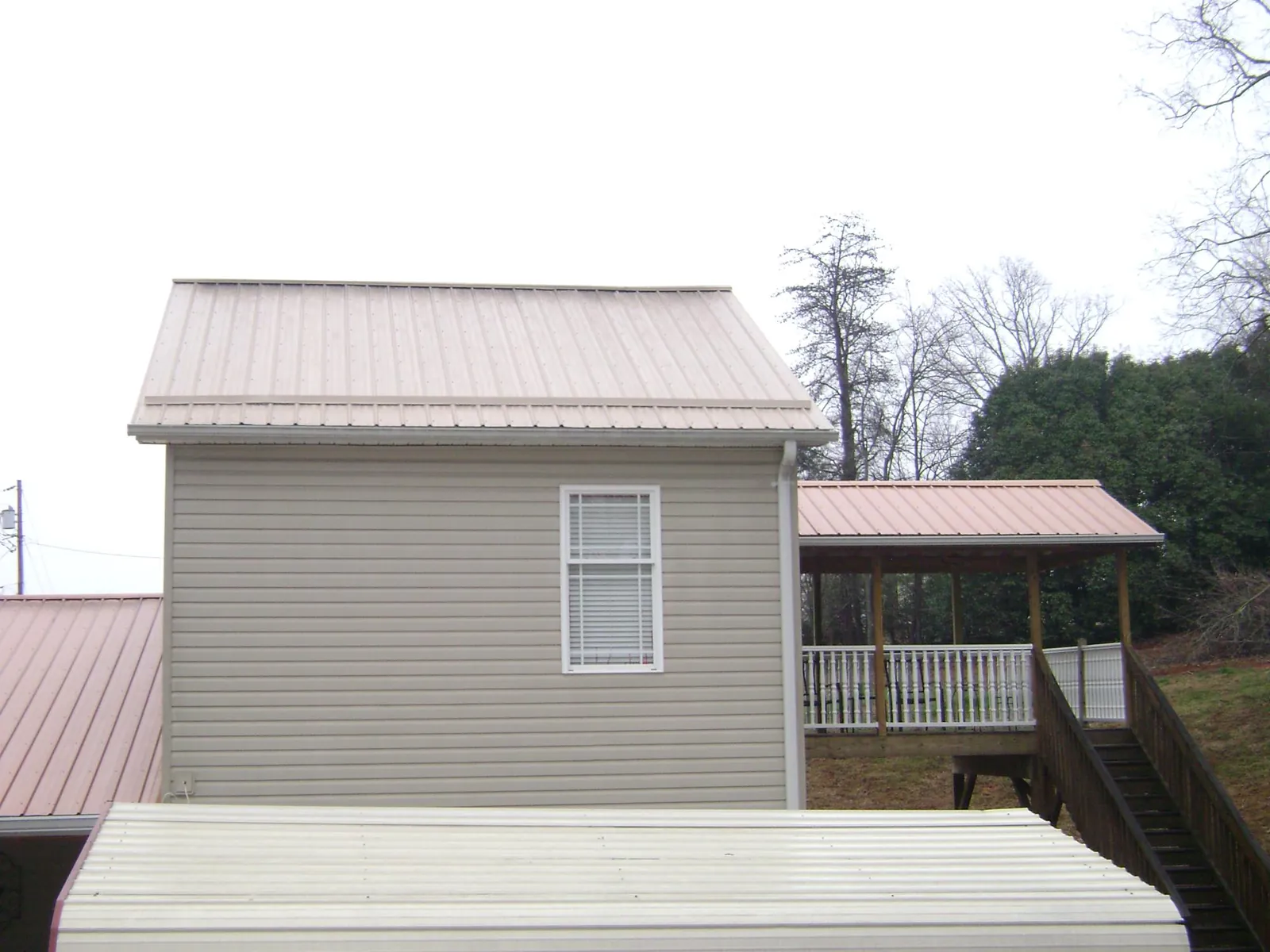 Tan metal roofs on a two story addition and attached porch, from a Roof Replacement job in Tetonia